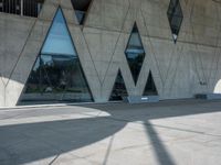 a building with some glass windows and a concrete floor with benches on it and the entrance is large and gray