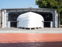 large white structure sitting on top of brick in a parking lot next to a tree