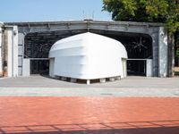 large white structure sitting on top of brick in a parking lot next to a tree