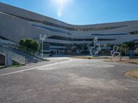 an empty parking lot with a staircase going up to the top and a curved building in the background