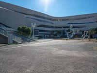 an empty parking lot with a staircase going up to the top and a curved building in the background