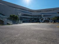 an empty parking lot with a staircase going up to the top and a curved building in the background