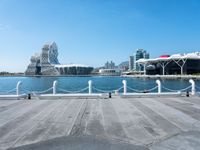 an empty pier on a bright day with the city of vancouver in the distance and some buildings in the background