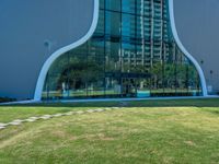 a green lawn in front of a building with an abstract shape on it and stairs to the side of it