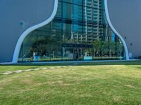 a green lawn in front of a building with an abstract shape on it and stairs to the side of it