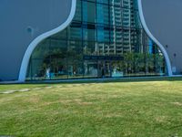 a green lawn in front of a building with an abstract shape on it and stairs to the side of it