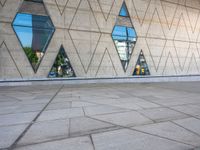 a sidewalk in front of an art museum with geometric windows and concrete tiles on the side of the building