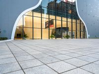 a building with multiple large glass windows reflecting it in the middle of a sidewalk of tiles