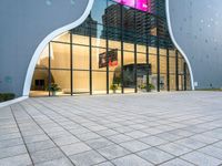 a building with multiple large glass windows reflecting it in the middle of a sidewalk of tiles