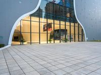 a building with multiple large glass windows reflecting it in the middle of a sidewalk of tiles