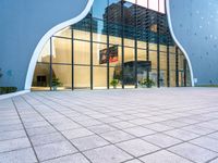 a building with multiple large glass windows reflecting it in the middle of a sidewalk of tiles