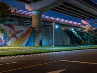 the painted mural above the highway on the side of a building at night with cars driving underneath