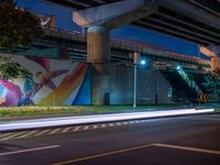 the painted mural above the highway on the side of a building at night with cars driving underneath