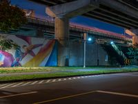 the painted mural above the highway on the side of a building at night with cars driving underneath