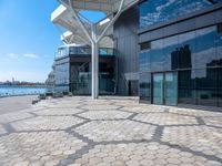 large open space, with the water in view outside of a building that has many windows and a large circular patio on one side of it