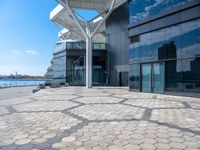 large open space, with the water in view outside of a building that has many windows and a large circular patio on one side of it