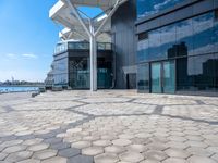 large open space, with the water in view outside of a building that has many windows and a large circular patio on one side of it