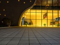 large square tile area with large glass doors in dark room with lights on windows on either side of the building