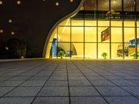 large square tile area with large glass doors in dark room with lights on windows on either side of the building