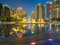 a rainy city street with tall buildings reflecting in it's water at nighttime