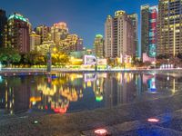 a rainy city street with tall buildings reflecting in it's water at nighttime