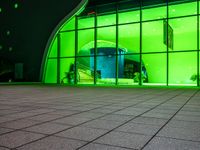 a green lit building with windows and stairs outside it and lights on outside the door