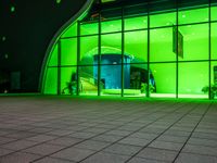 a green lit building with windows and stairs outside it and lights on outside the door