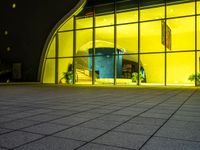 a building has glass windows and plants on the outside and outside of it at night