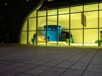 a building has glass windows and plants on the outside and outside of it at night