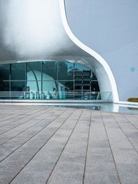 an image of outside view of a building with glass walls and a pool on the ground
