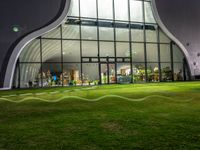 an illuminated building that is outside at night in grass field with lawn and windows filled with wine