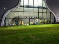 an illuminated building that is outside at night in grass field with lawn and windows filled with wine