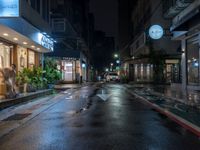 an empty city street during the rain in the night time with a person passing through it