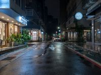 an empty city street during the rain in the night time with a person passing through it