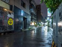 a wet street with graffiti on it next to a wall with a smiling face painted on it