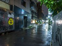 a wet street with graffiti on it next to a wall with a smiling face painted on it