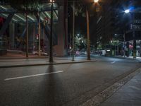 a deserted street at night in a city with several trees and tall buildings with lights hanging on top