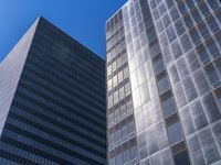 two tall glass skyscrapers in a city setting with the sky above them, all on a blue sunny day