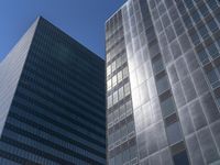 two tall glass skyscrapers in a city setting with the sky above them, all on a blue sunny day