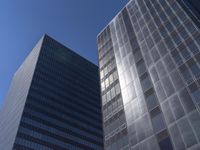 two tall glass skyscrapers in a city setting with the sky above them, all on a blue sunny day