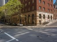 there is a very tall red brick building on the corner of the street with cars parked along it