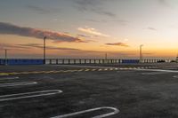 a parking lot with lines painted on it as the sun sets over the water and in the distance, near an ocean