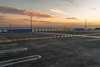 a parking lot with lines painted on it as the sun sets over the water and in the distance, near an ocean