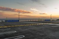 a parking lot with lines painted on it as the sun sets over the water and in the distance, near an ocean