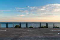 the fence and the road are in front of the water with some clouds in the sky