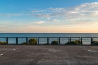 the fence and the road are in front of the water with some clouds in the sky