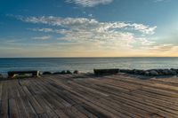 an empty wooden deck overlooking the ocean on a sunny day with the sun setting behind