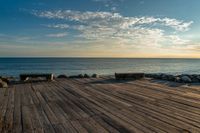 an empty wooden deck overlooking the ocean on a sunny day with the sun setting behind