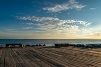 an empty wooden deck overlooking the ocean on a sunny day with the sun setting behind