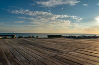 an empty wooden deck overlooking the ocean on a sunny day with the sun setting behind